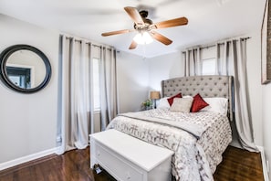 A bedroom with a large bed, a ceiling fan, a round mirror, and a bedside table with a lamp.