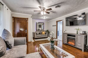 A living room with a sofa, a coffee table, a fireplace, and a ceiling fan.