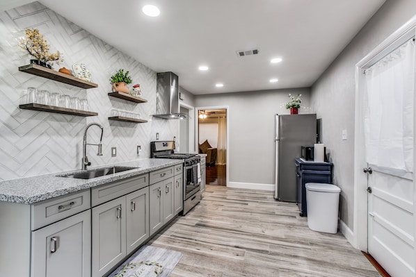A modern kitchen with a herringbone tile backsplash, stainless steel appliances, and built-in shelves.