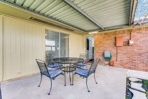 A covered patio with a round table and chairs, a brick wall, and a window with blinds.
