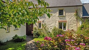 Een stenen huis met een metselstenen dak, een voordeur en een kleine tuin met roze bloemen.