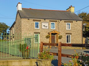 Un bâtiment en pierre avec une enseigne indiquant le pub « The Farmers Arms », une porte en bois et un portail métallique vert.