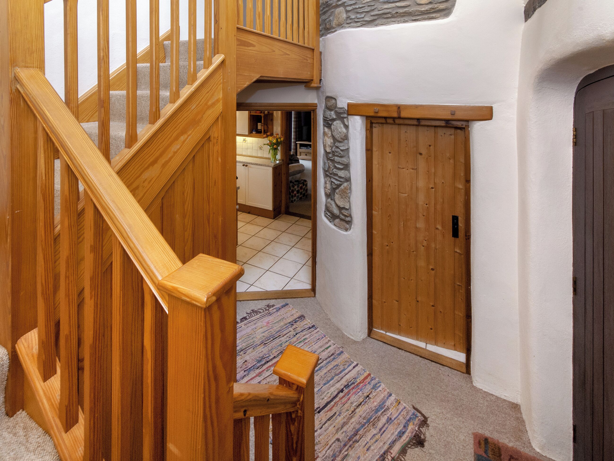 A wooden staircase leading to a kitchen area with a stone accent wall and a wooden door.