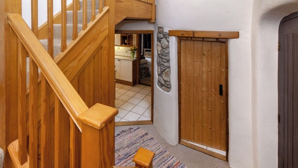 Een houten trap die leidt naar een keuken met een steen accentmuur en een houten deur.