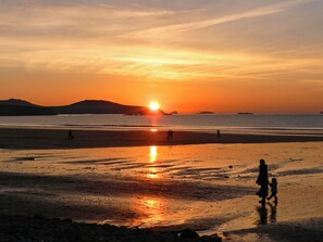 A beach scene with a sunset, people walking, and distant mountains.