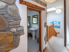 A stone wall, a wooden door, a bathroom with a sink and mirror, a patterned floor, a staircase with a railing, and a painting on the wall.