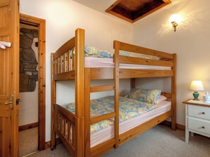 A bunk bed with a wooden frame, a nightstand with a lamp, and a door with a stone wall.