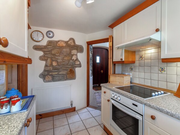 A kitchen with a stone wall, a stove, and a door leading to another room.