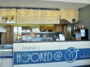A menu board with Welsh Ice Cream and Hooked @ 31 branding, a coffee machine, and a counter with various food items.