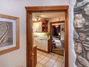 A hallway leading to a kitchen with a tiled floor, wooden cabinets, a toaster, and a vase with flowers.