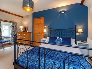 A bedroom with a bed, bedside lamps, a wooden dresser, a chair, and a window with curtains.