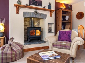 A cozy living room with a stone fireplace, a comfortable armchair, a plaid armchair, and a coffee table with a book. - 2 bedroom accommodation in Castlemorris (Castlemorris)