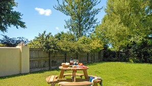 Een picknickopstelling met een houten tafel, stoelen en een mand op een gazon.