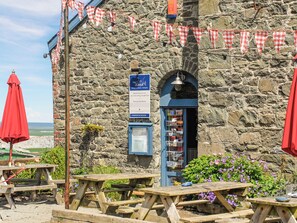 A stone building with a blue signboard, picnic tables, and red umbrellas. - 2 bedroom accommodation in Castlemorris (Castlemorris)