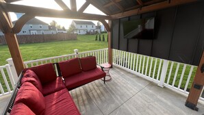 En overdækket terrasse med en rød sofa, et lille bord og et tv-skærm.