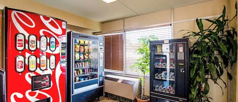 A vending area with Coca-Cola and Sprite machines, a potted plant, and a window with blinds.