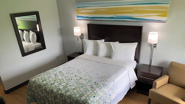 Une chambre d’hôtel avec un grand lit, deux tables de chevet, une chaise, une petite table et un miroir fixé au mur.