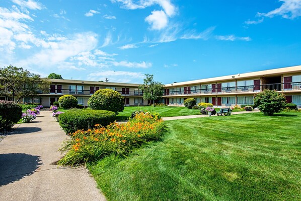 A two-story motel with a well-maintained lawn, a pathway, and a small garden area with flowers. - HomeTowne Studios by Red Roof Battle Creek (Battle Creek)