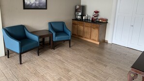 Une pièce avec deux fauteuils bleus, une petite table, un meuble en bois contenant des appareils de cuisine et une porte blanche.