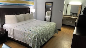 A hotel room with a bed, bedside table, lamp, mirror, and a bathroom with a sink and mirror.