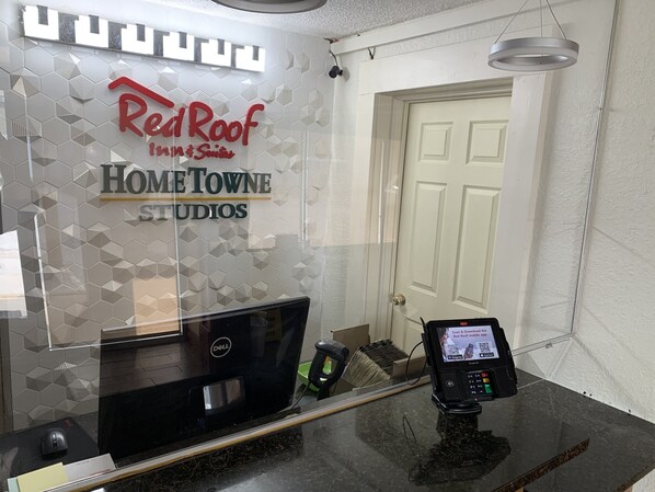 A reception desk with a computer, a payment terminal, and a Red Roof Inn & Suites sign. - HomeTowne Studios by Red Roof Battle Creek (Battle Creek)