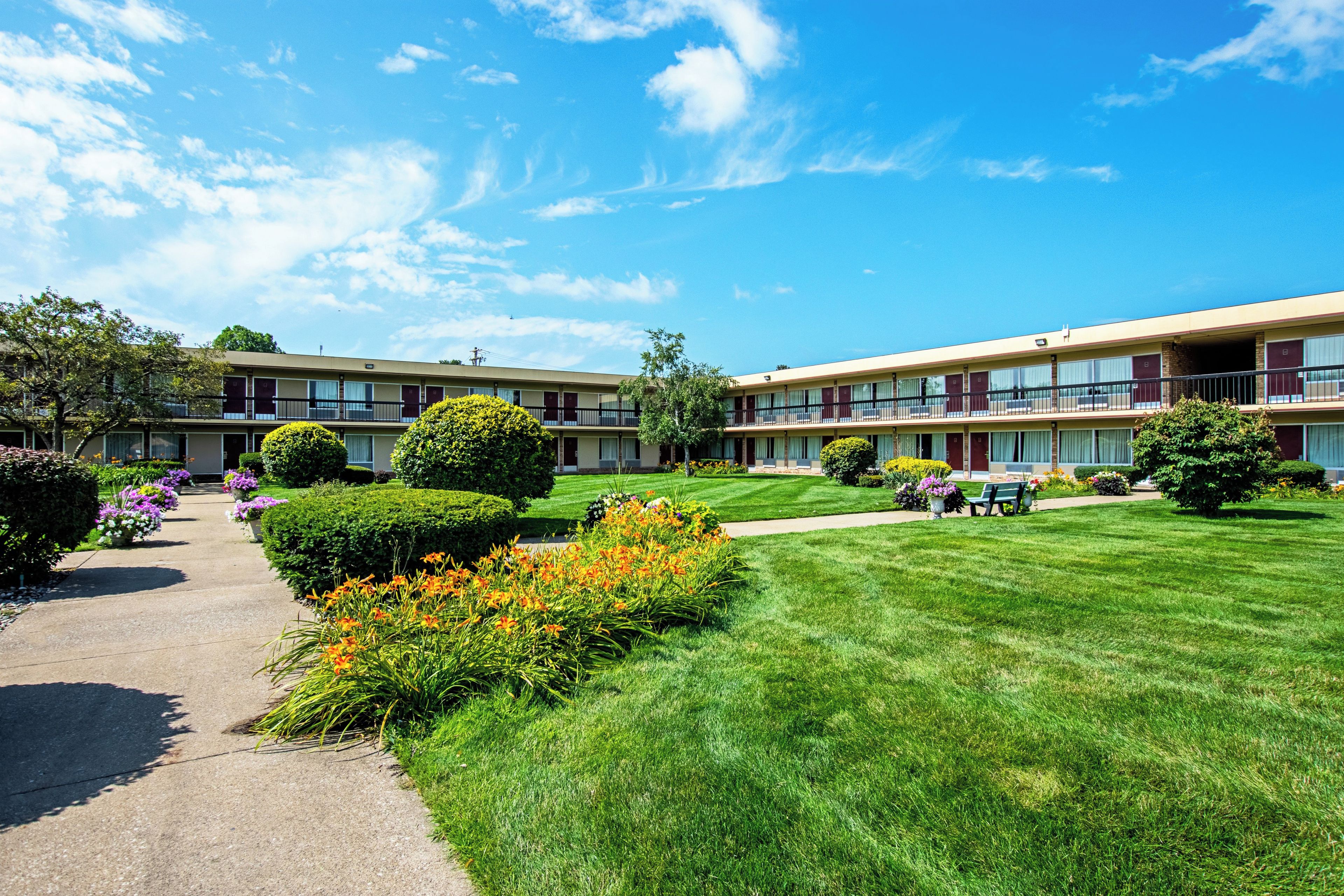 A two-story motel with a well-maintained lawn, a pathway, and a small garden area with flowers.