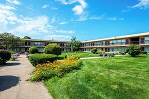 Ein zweistöckiges Motel mit gepflegtem Rasen, einem Weg und einer kleinen Blumenrabatte.