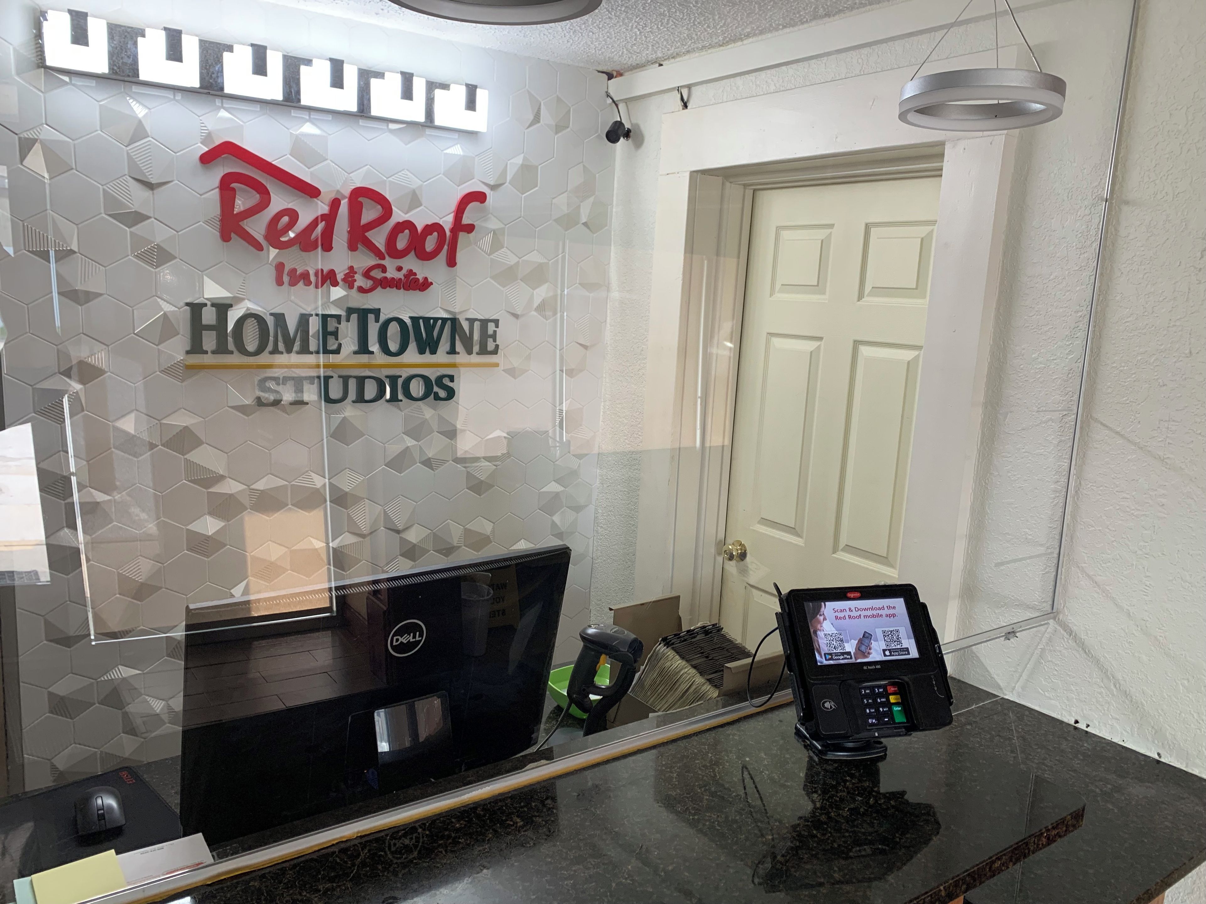 A reception desk with a computer, a payment terminal, and a Red Roof Inn & Suites sign.