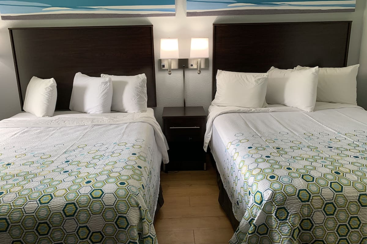 Hotellihuone, jossa on kaksi sänkyä, yöpöytä, seinään kiinnitetty lamppu ja taulu sänkyjen yläpuolella.