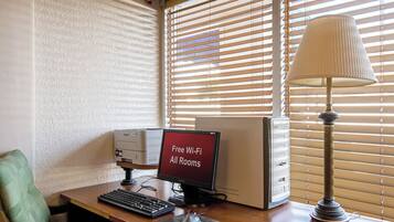 A computer desk with a monitor displaying "Free Wi-Fi All Rooms," a keyboard, a mouse, and a lamp.