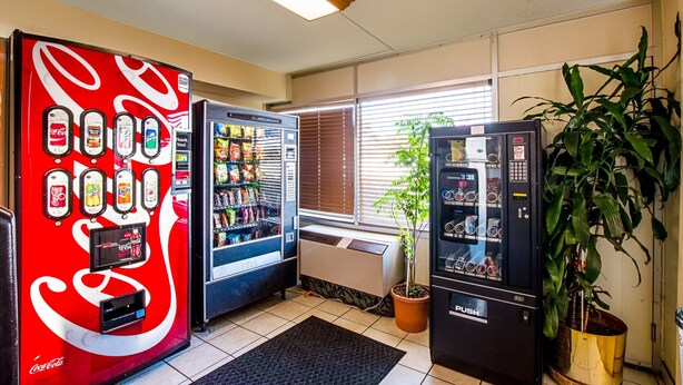 Un espace de vente proposant des distributeurs automatiques de Coca-Cola et de Pepsi, un distributeur de boissons et une plante en pot.