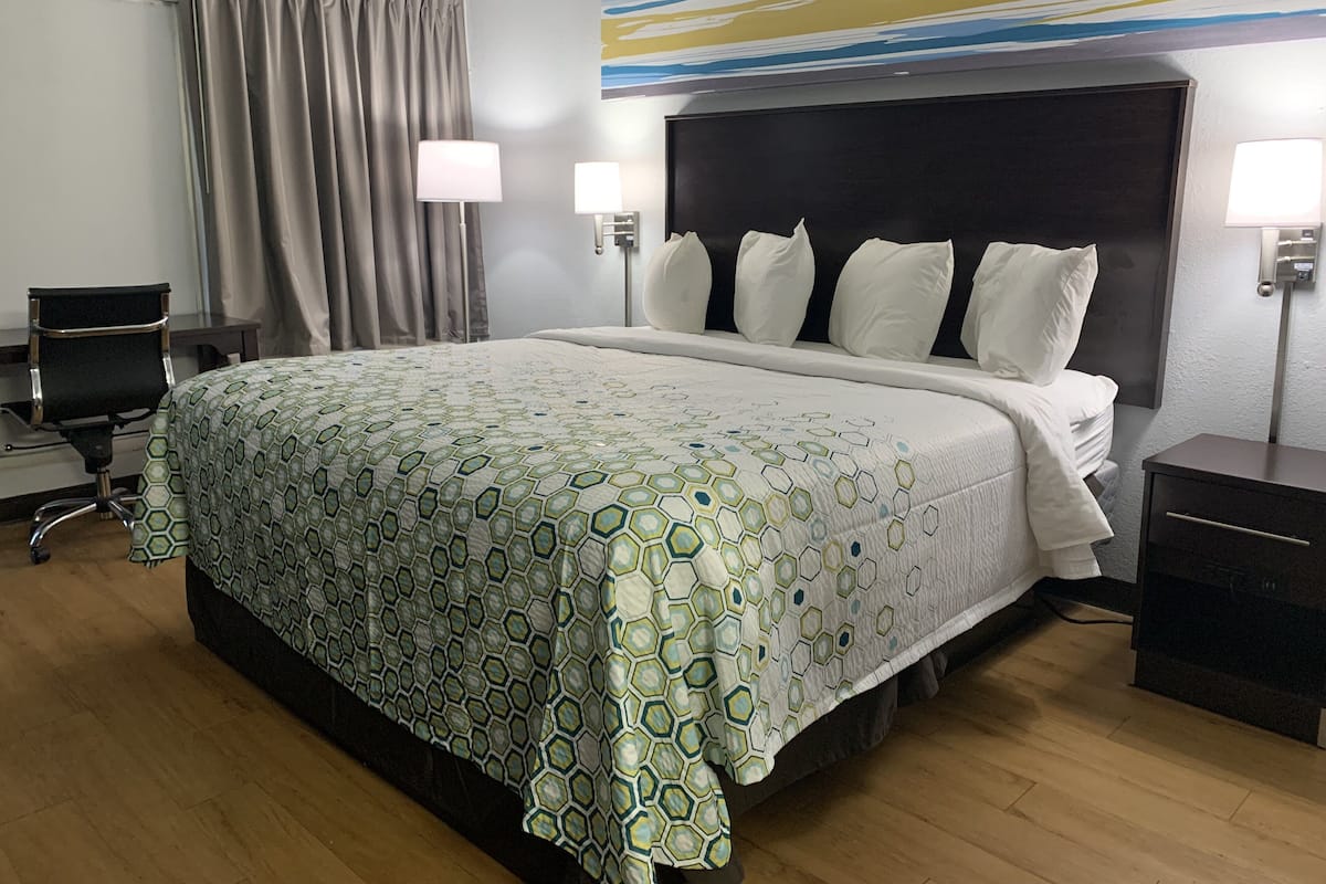 Hotellihuone, jossa on suuri sänky, kaksi yöpöytävalaisinta, työpöytä ja tuoli.