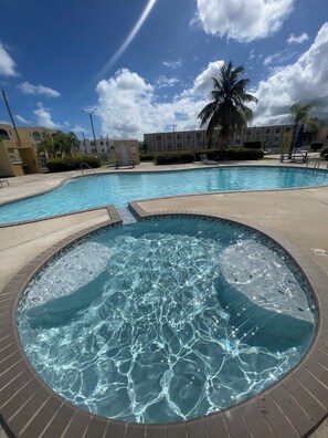 A swimming pool with a hot tub, surrounded by a building with balconies and palm trees. - Cozy and Peaceful place-Rio Grande-El Yunque Rainforest  (Río Grande)
