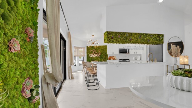 Una cocina moderna con armarios blancos, una isla central y un jardín vertical verde.