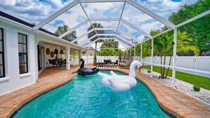 Una piscina con dos cisnes inflables y una ballena orca, rodeada por un porche cubierto con mobiliario exterior.