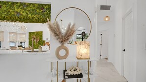 Un interior moderno con una paleta de colores blancos, un espejo decorativo, una planta en la pared y una exhibición de objetos esféricos.