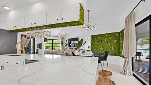 Una cocina moderna con gabinetes blancos, encimera de mármol y una pared jardín vertical verde.