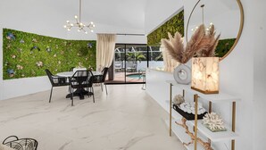 Un comedor moderno con una mesa y sillas blancas, una pared verde con adornos florales, un espejo grande y un jarrón decorativo.