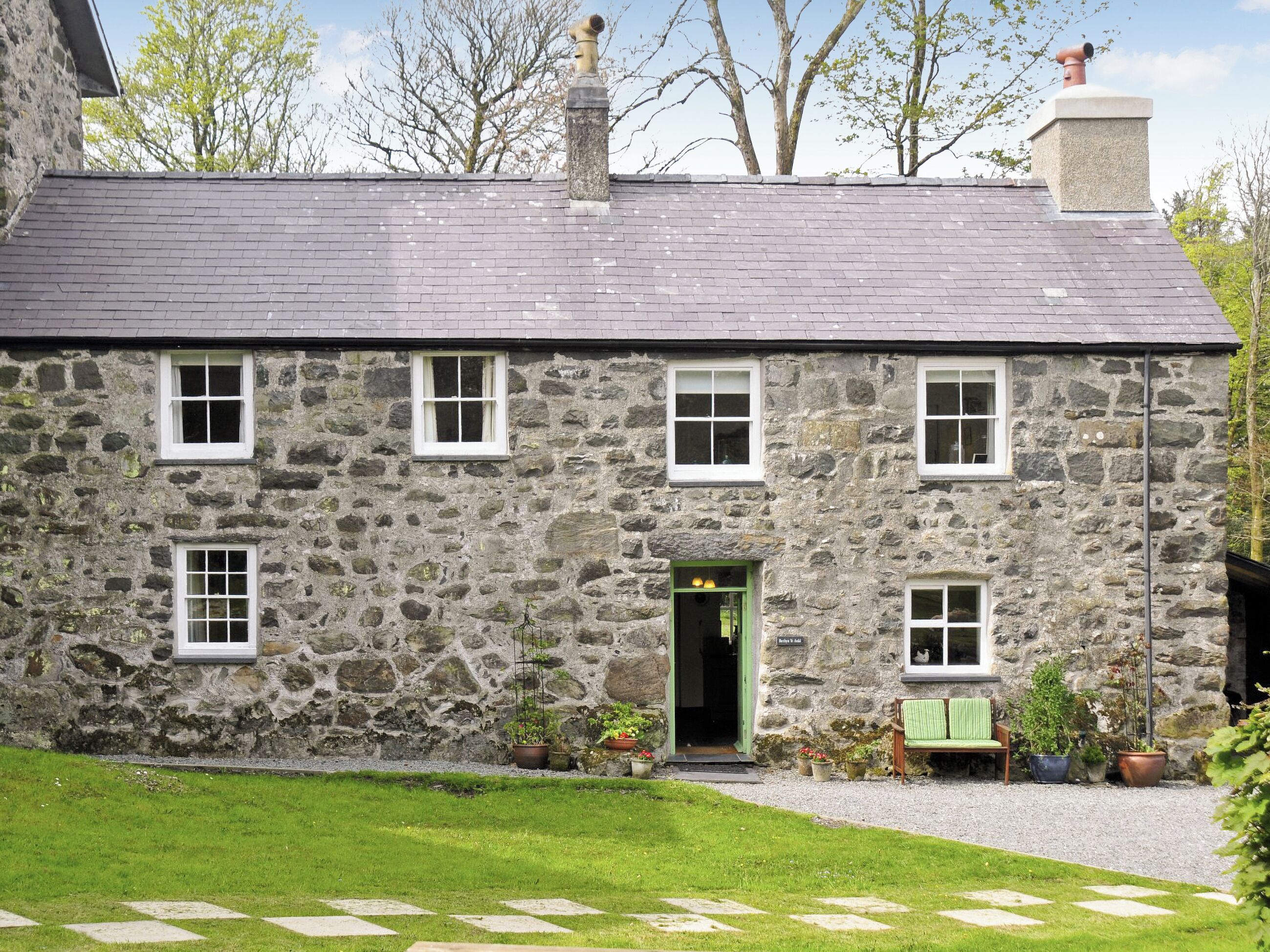 A stone building with a slate roof, multiple windows, and a green door.