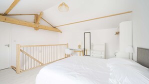A bedroom with a large bed, a desk, a wardrobe, and a sloped ceiling with exposed beams. - Apartment Comfortable in the centre of Pau: parking, AC... (Pau)