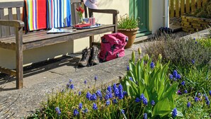 Un banc en bois, recouvert d’une couverture à rayures, avec un chapeau et un sac rose à côté.