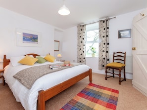 A bedroom with a bed, a chair, a window with curtains, a lamp, and a framed picture on the wall.