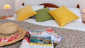 Un lit bien fait, avec des oreillers, un chapeau de paille et des magazines de voyage, le tout posé sur un tapis.