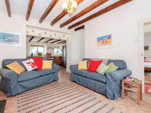A living room with two sofas, a patterned rug, wooden beams, and artwork on the walls.