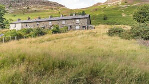 Ein Steinhaus mit zahlreichen Fenstern und einem geneigten Dach, umgeben von grünen Feldern und Hügeln.