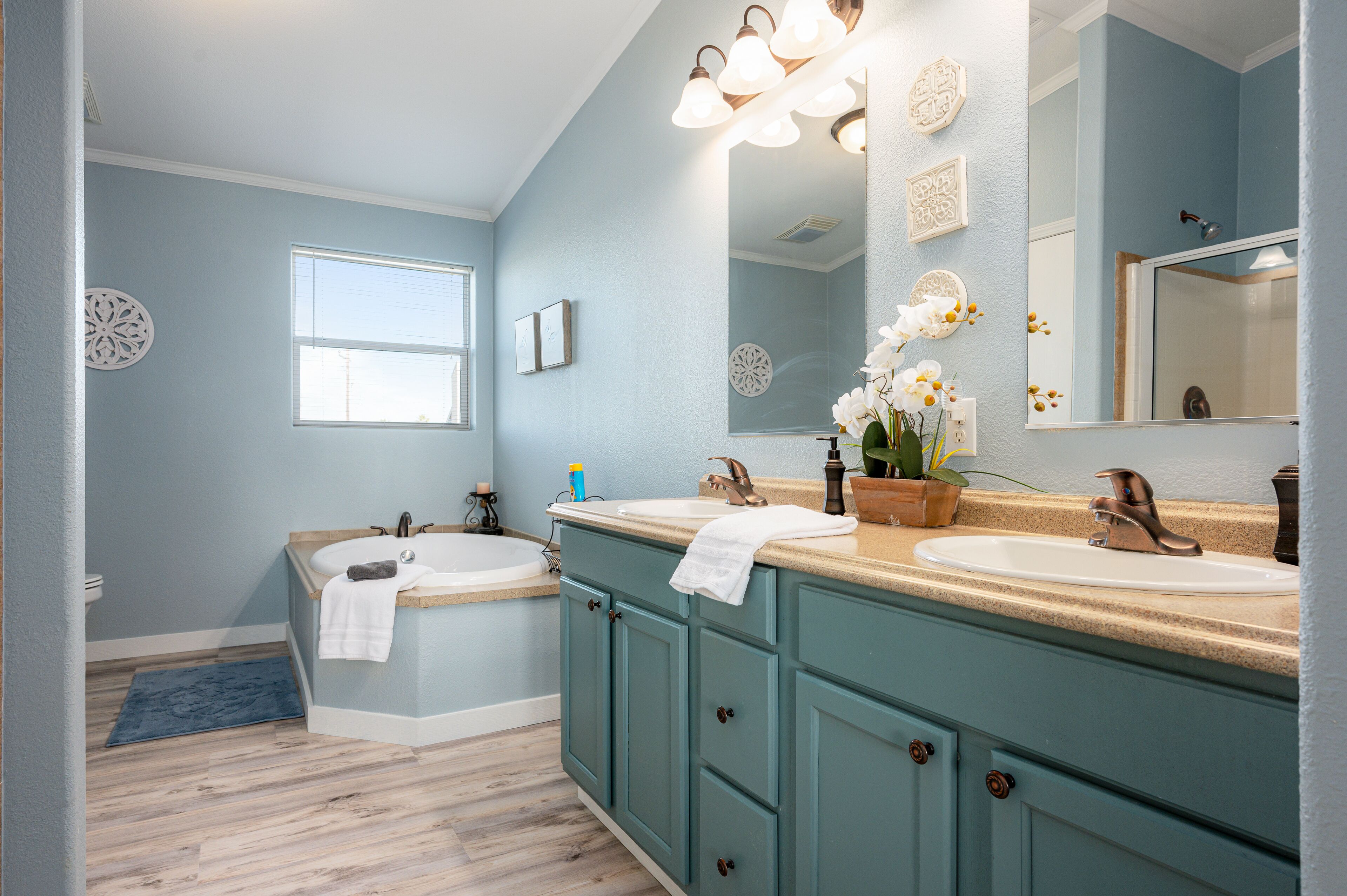 Un bagno con due lavandini, una vasca e un grande specchio. Luci decorative sopra gli specchi e una finestra che lascia entrare luce naturale.