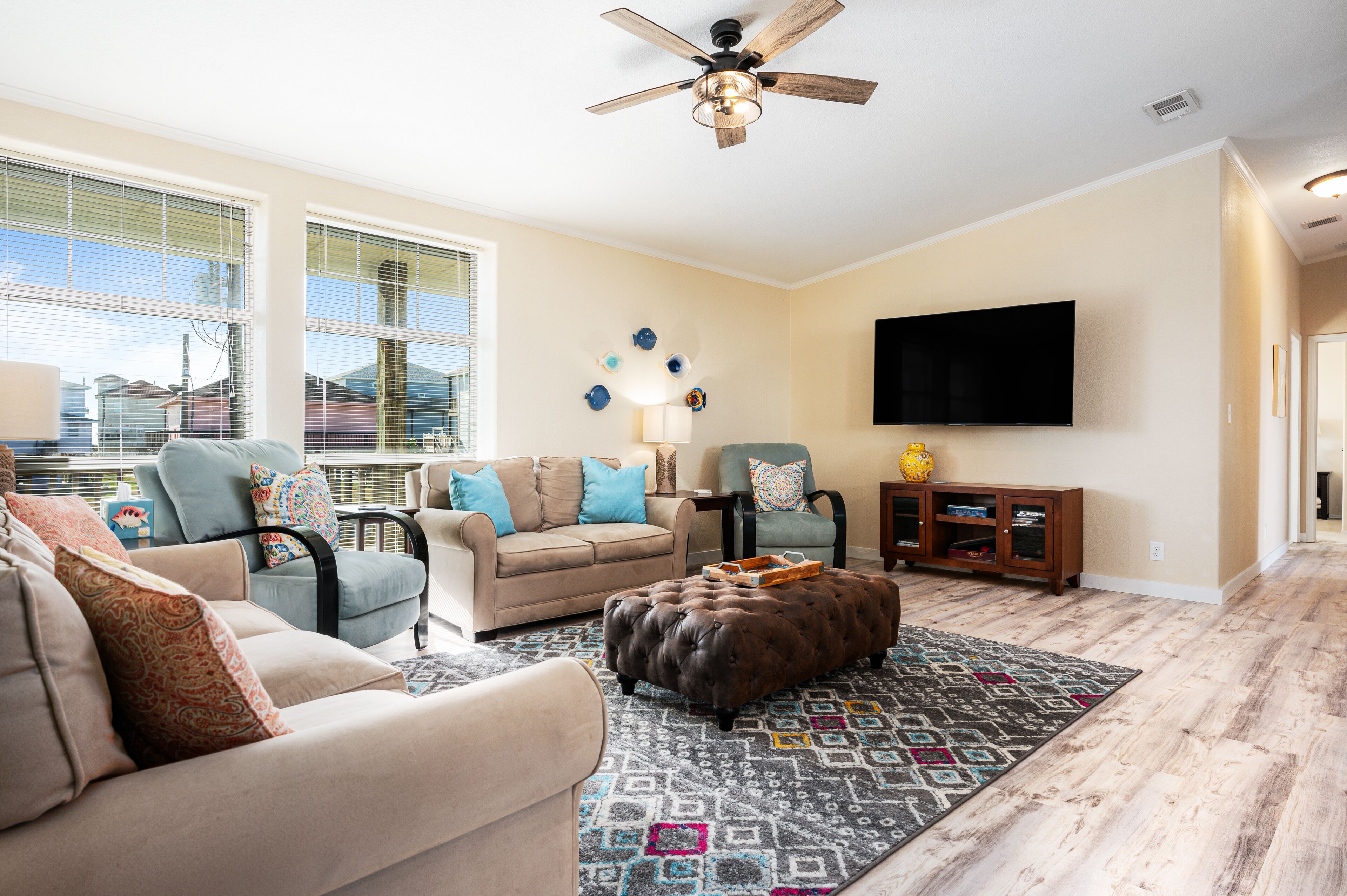 Un salon avec un canapé beige, un fauteuil bleu, un pouf marron et un tapis à motifs.