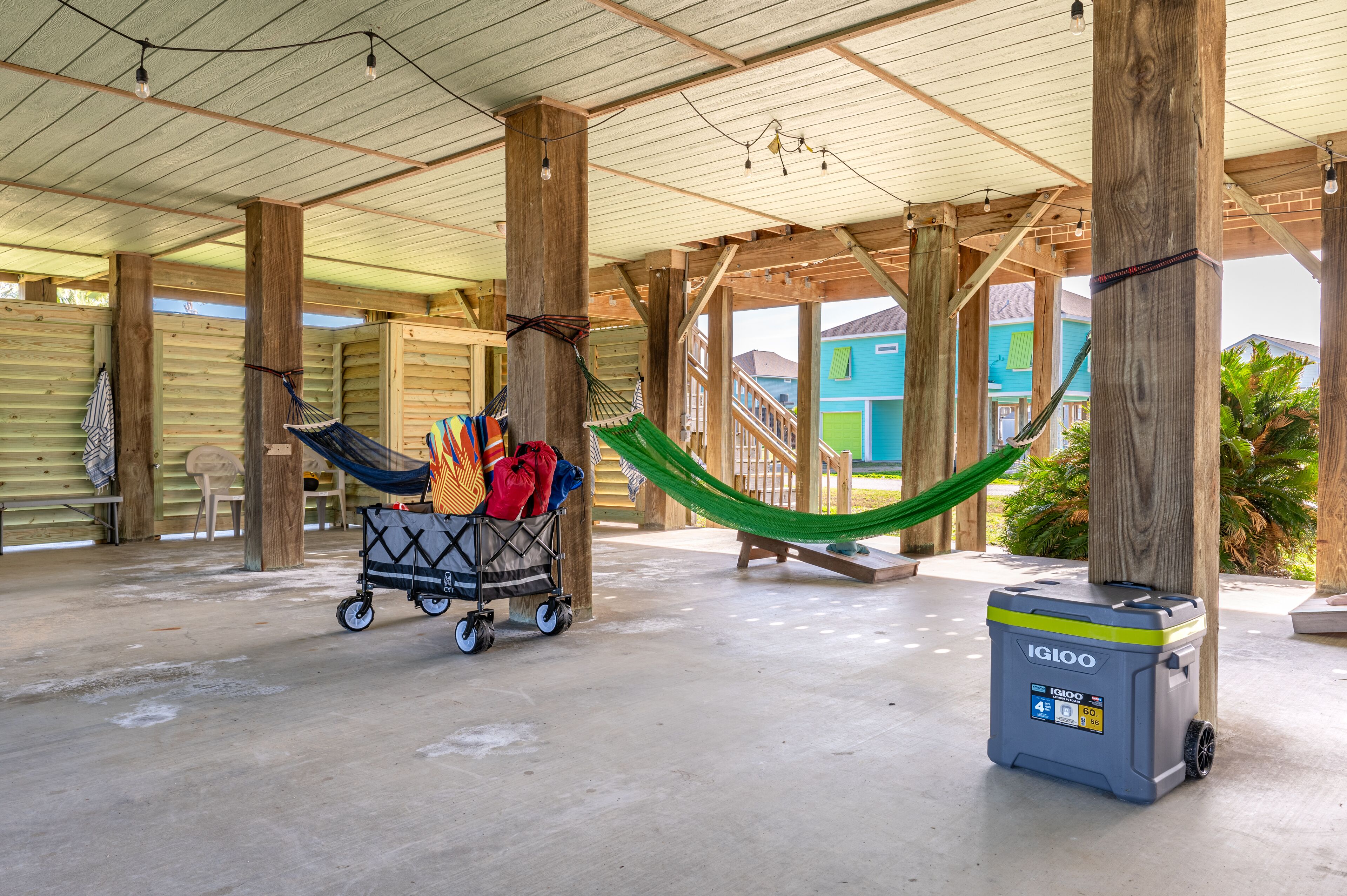 A covered outdoor area with wooden pillars, a hammock, a cart with bags, and a portable cooler.