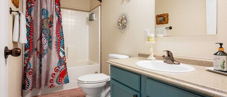 A bathroom with a shower curtain, toilet, sink, and vanity.