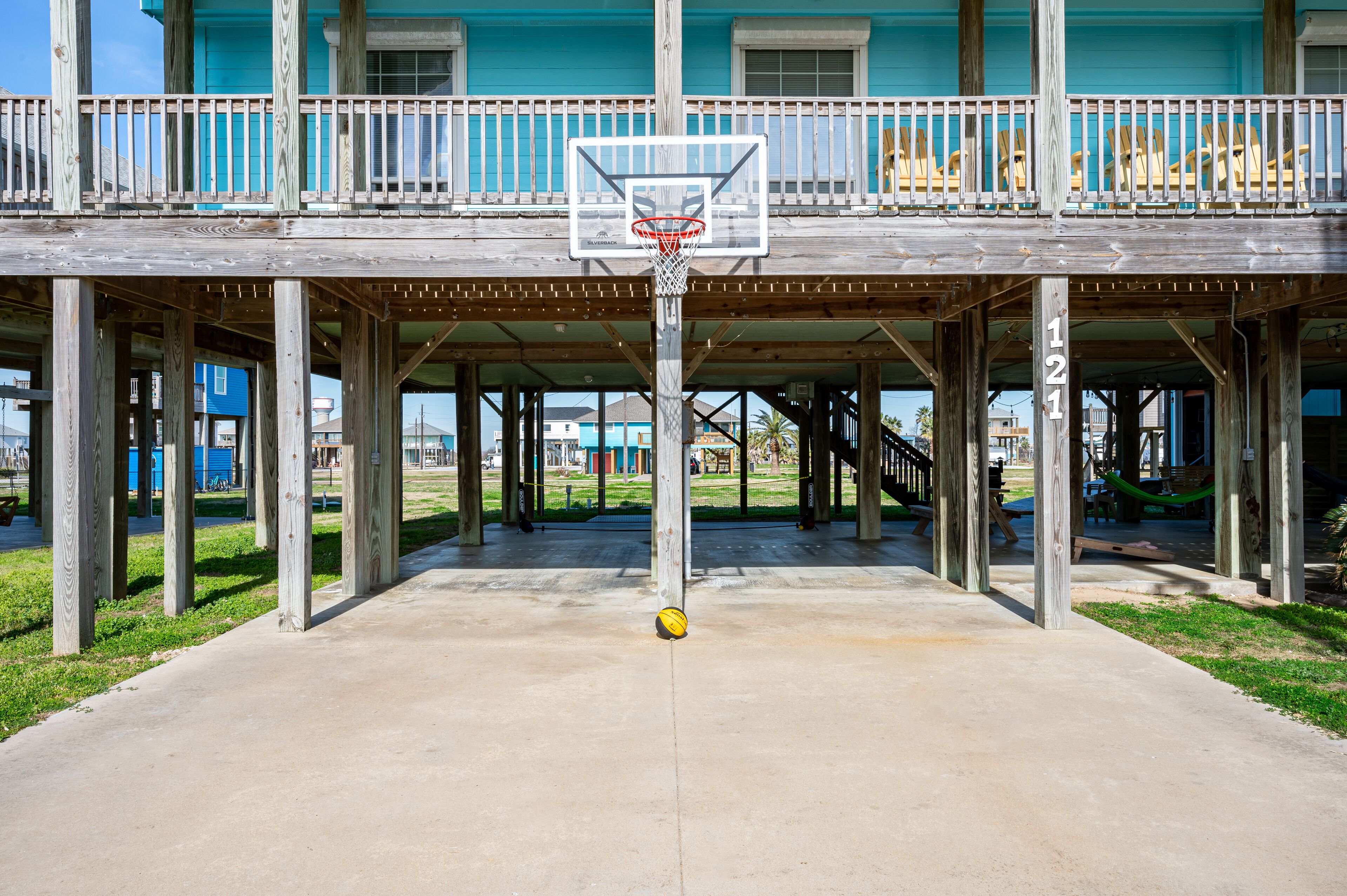 Ein Basketballplatz mit Korb vor einer Holzterrasse mit Balkon.
